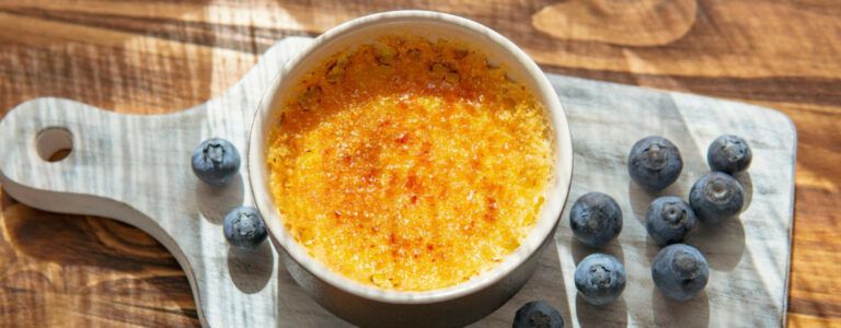 une creme brulée sur un plan de travail entourée de baie de myrtilles