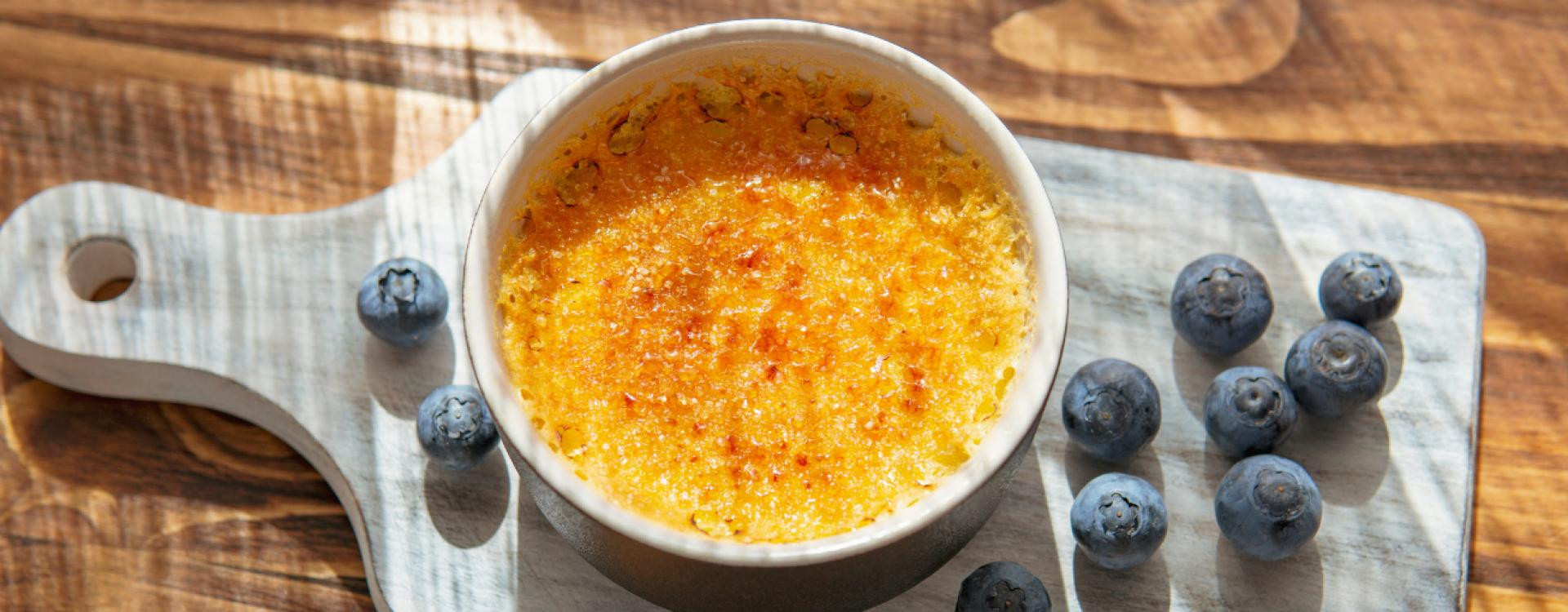 une creme brulée sur un plan de travail entourée de baie de myrtilles